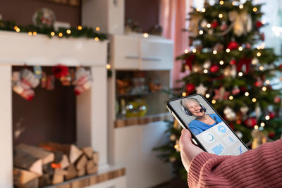 Midsection of person holding mobile phone on christmas tree