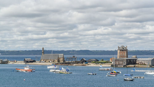 Sailboats moored on sea against sky in city