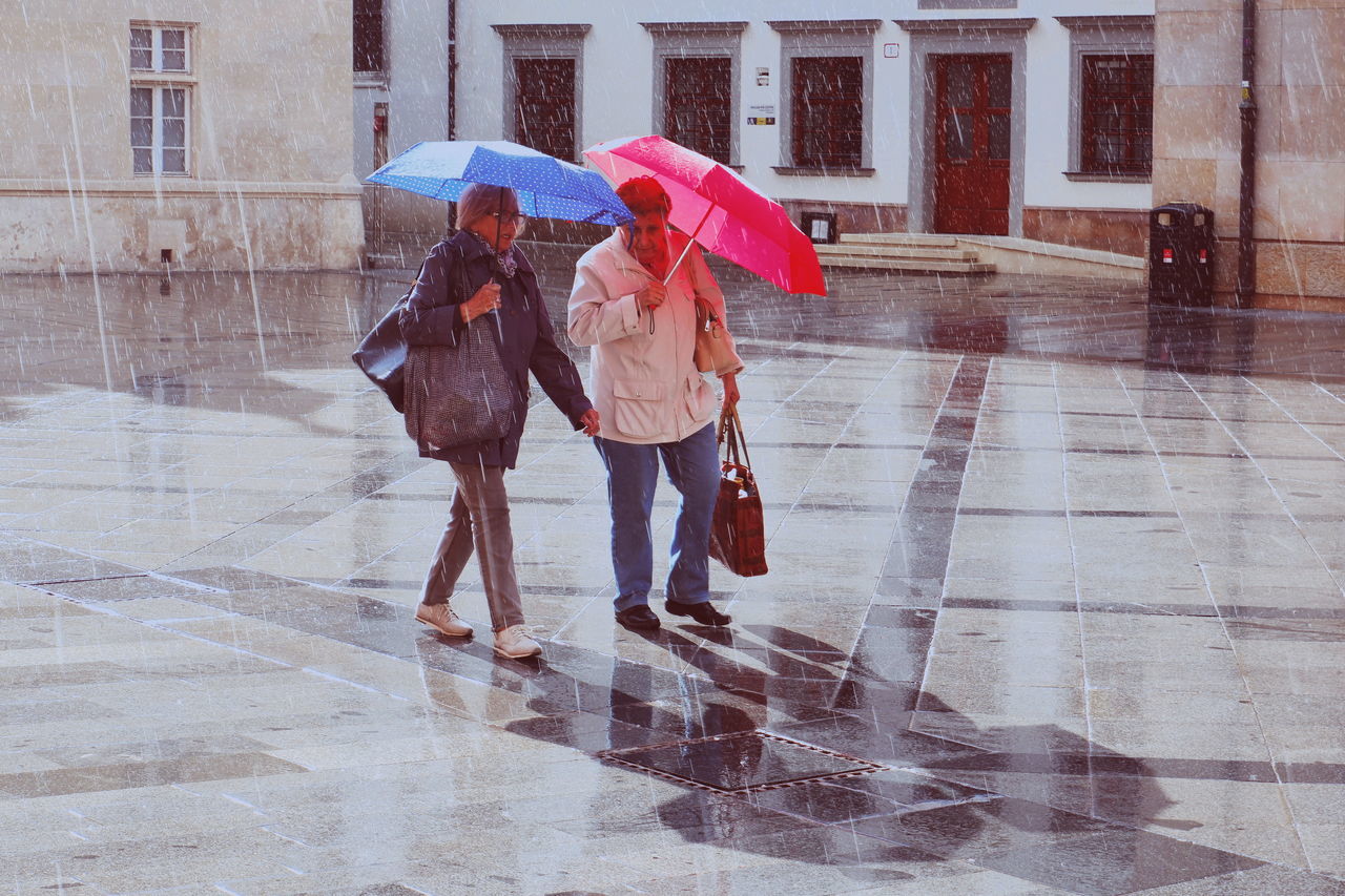rain, umbrella, wet, walking, women, city, architecture, adult, protection, full length, street, real people, lifestyles, people, two people, city life, men, security, built structure, rainy season, positive emotion, outdoors