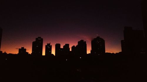 Silhouette buildings in city against sky at night