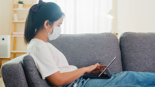 Young woman using phone while sitting on sofa