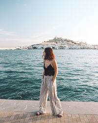 Rear view of young woman standing by sea against sky
