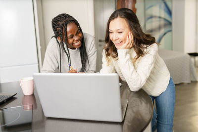 Smiling young women using laptop on table at home