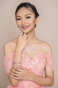 Close-up portrait of happy beautiful woman wearing peach dress against beige background