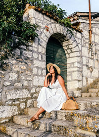 Attractive young woman in white dress sitting on stairs in old town. lifestyle, summer.