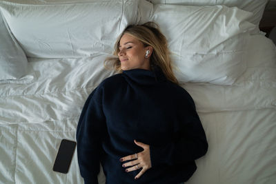 Woman listens to music with headphones in her bed in her apartment. mobile phone, technology.