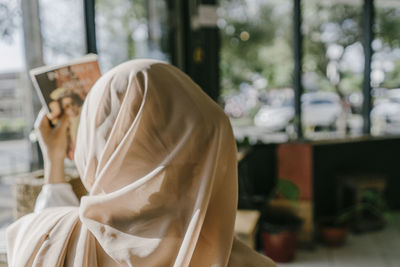Portrait of woman holding mobile phone and book. hijab girl at the coffee shop from behind. 