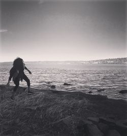 Woman throwing stone in sea against sky