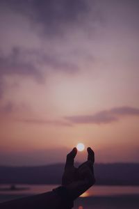 Optical illusion of hand holding sun at beach during sunset