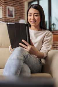 Smiling woman using tablet pc sitting on sofa at home