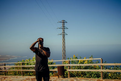 Man standing by electricity pylon against sky