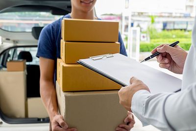 Cropped hands of woman signing in paper while delivery man holding cardboard boxes