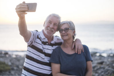 Young man photographing woman using smart phone at beach