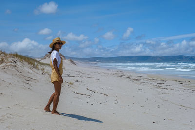 Side view of woman standing at beach against sky