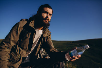 Full length of young man sitting on land against clear blue sky