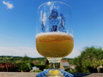 Close-up of beer glass on table against blue sky