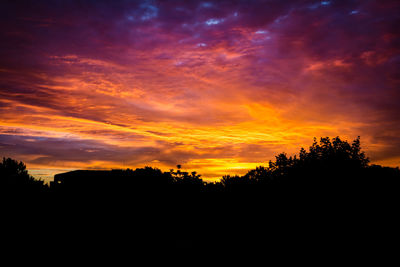 Silhouette trees against dramatic sky during sunset
