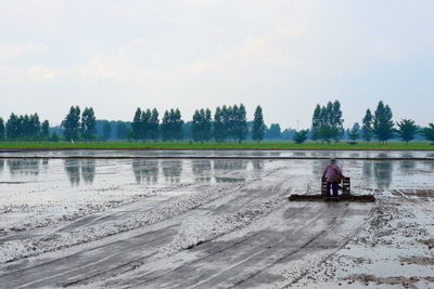 Man sitting by lake against sky