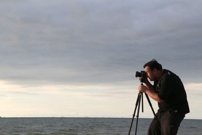 Man photographing at beach against sky