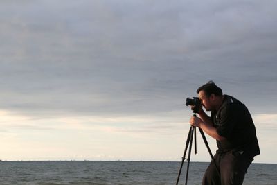 Man photographing at camera against sky