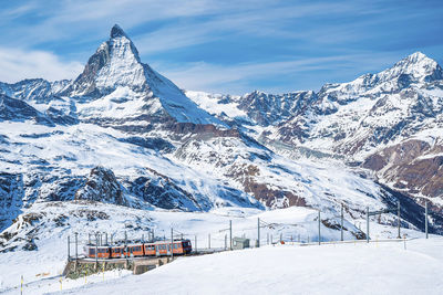 Red train climbing up to gornergrat station with view of matterhorn against sky