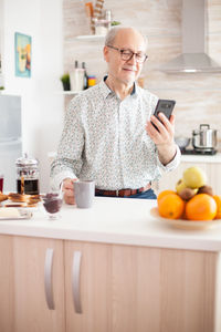 Senior man using mobile phone at kitchen