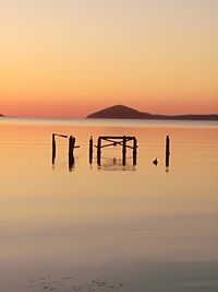 Silhouette wooden posts in sea against sky during sunset