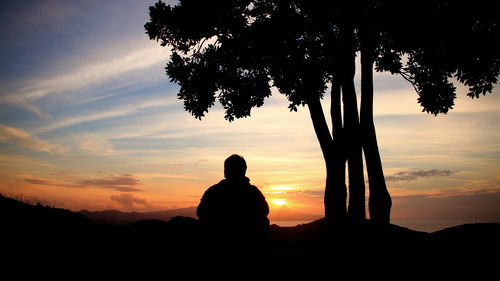 Silhouette people sitting on mountain against sky during sunset