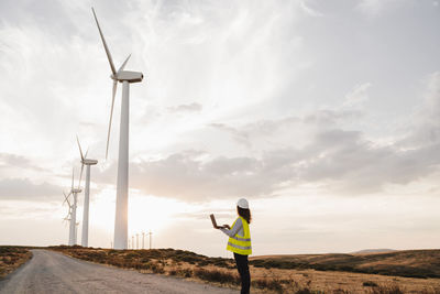 Engineer looking at wind turbines at wind farm on sunset