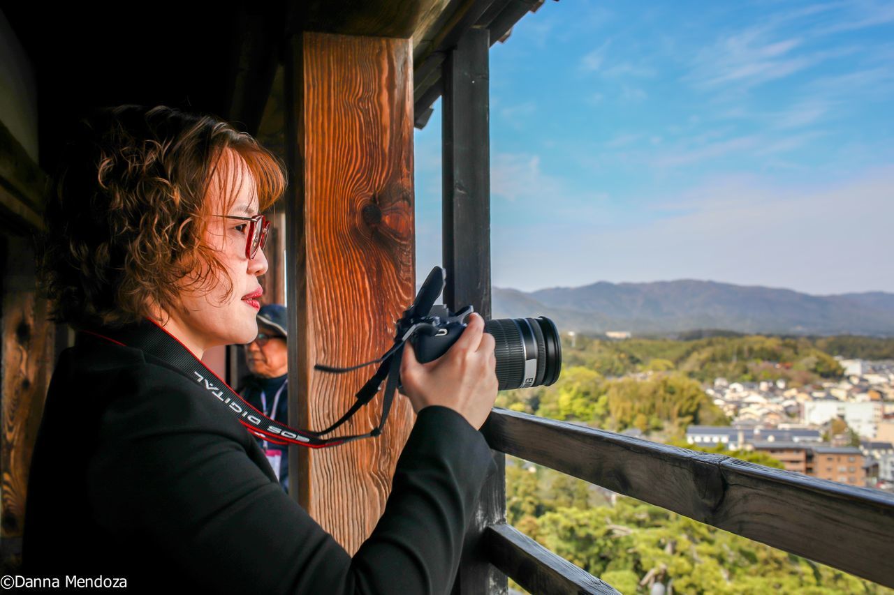 PORTRAIT OF SMILING WOMAN HOLDING CAMERA WHILE PHOTOGRAPHING