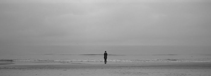 Rear view of woman standing at beach against sky