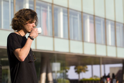 Young man drinking coffee while standing against building