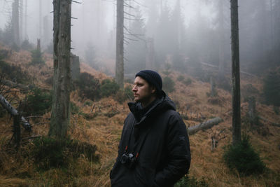 Young man looking away while standing in forest