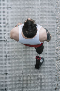 From above young guy with leg prosthesis running up paved slope against shabby building during workout on city street