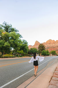 Rear view of woman walking on road against clear sky