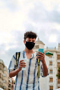 Young afro man with mask is walking while he is using his phone