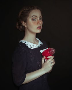Portrait of beautiful young woman with toy standing black background