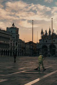 Rear view of people walking on street by buildings against sky