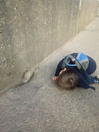 High angle portrait of man relaxing on footpath against wall