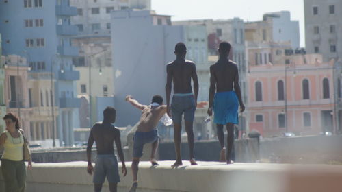 Rear view of shirtless teenagers walking on retaining wall against buildings