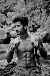 Shirtless young man with backpack sitting on rock outdoors