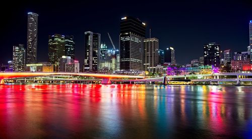 Illuminated buildings by river against sky at night