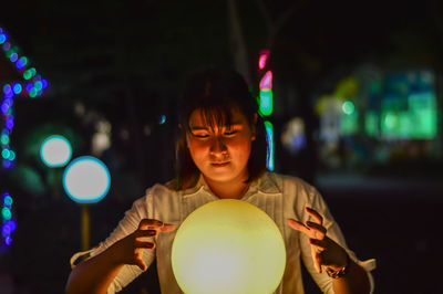 Woman with illuminated crystal ball at night