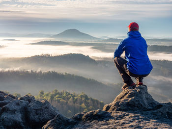 Nature adventure. hiker sit on the rock and watch over misty morning valley to rising sun at horizon
