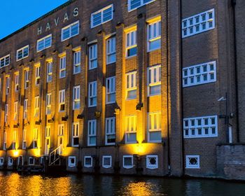 Illuminated buildings by river at dusk