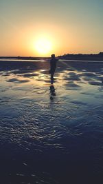 Silhouette person on beach against sky during sunset