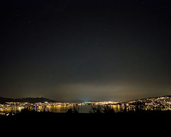 Illuminated buildings by sea against sky at night