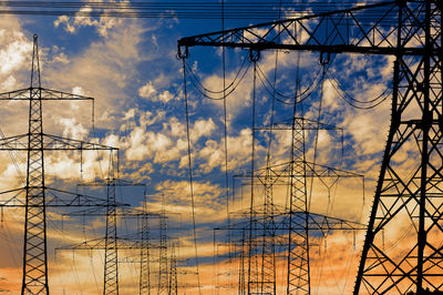 Low angle view of electricity pylons against sky during sunset