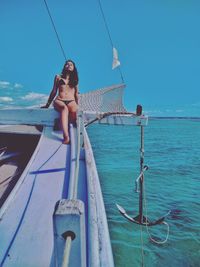 Woman wearing bikini sitting in boat on sea against sky