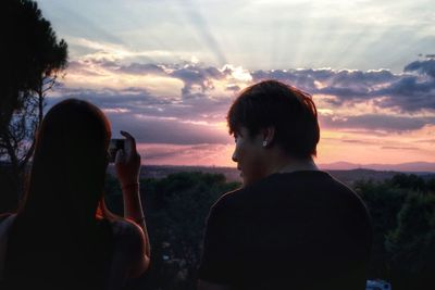 Portrait of woman photographing against sky during sunset